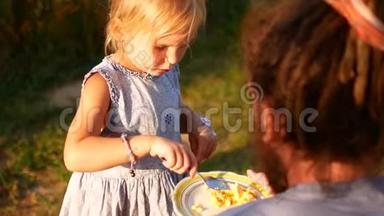 一个小女孩用勺子喂她爸爸。 在村子里的夏日夜晚
